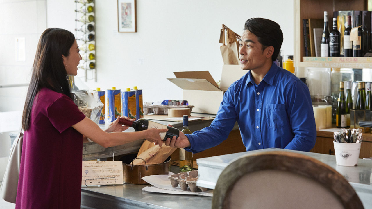 Male handing a bottle of wine to a female in a shop