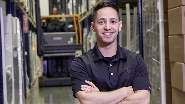 Male standing with folded arms in warehouse full of boxes