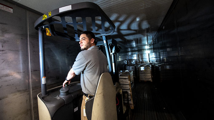 Male on a forklift pulling pallets of boxes from the back of a truck