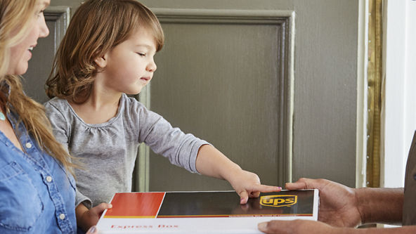 UPS driver handing a package to a female carrying her child as she points to the box