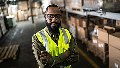 Male wearing a safety vest standing in a warehouse with arms folded
