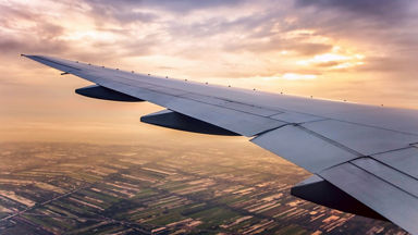 Airplane wing over land with the sunrise behind it