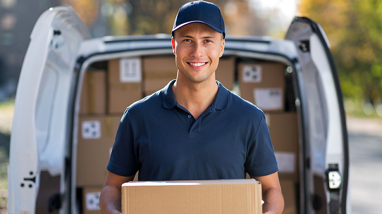 Male holding a box in front of a delivery van full of boxes