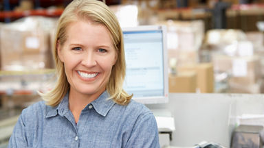 Female smiling at the camera in front of a computer and warehouse