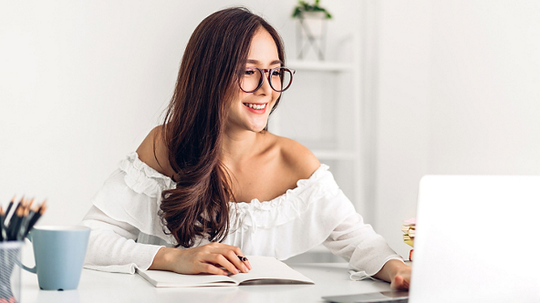 Female sitting at a desk with an open notebook and using a laptop