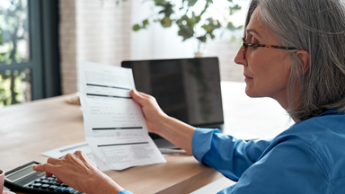 Woman looking at paper document and entering numbers in calculator