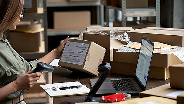 Female scanning the label of a package at a desk full of boxes