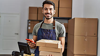 Male in an apron holding three boxes and his cell phone