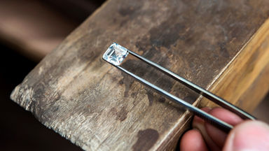 Tweezers holding a square diamond over wood 